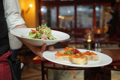 Server presenting two plated Italian dishes